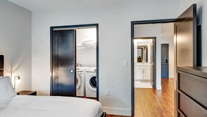 A modern hotel room with a bed, a nightstand, a washing machine, and a mirror.