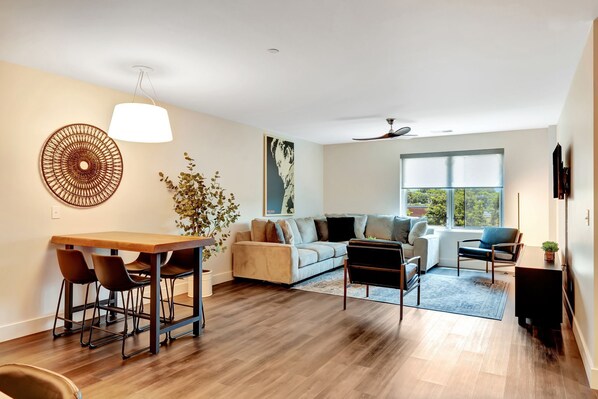 Una sala de estar moderna con una mesa de comedor de madera, un sofá y un ventanal grande.