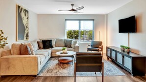 Een moderne woonkamer met een bank, salontafel, fauteuil en een televisie op een dressoir.