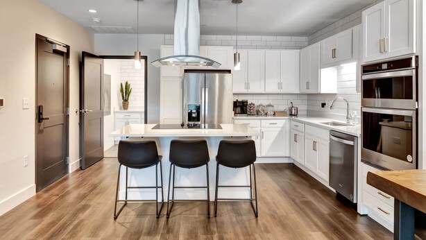 Een moderne keuken met witte kasten, roestvrijstalen apparatuur en een centraal eiland met barkrukken.