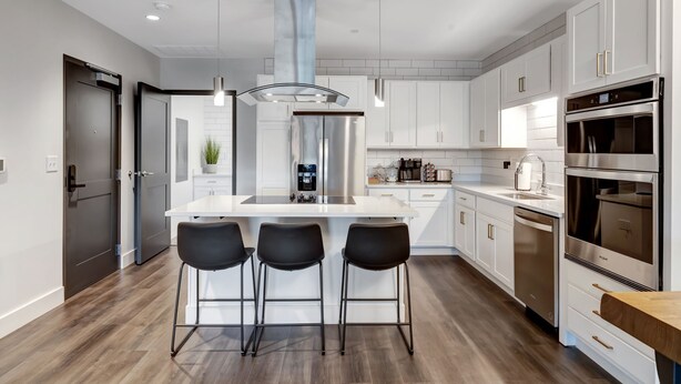 A modern kitchen with white cabinetry, stainless steel appliances, and a central island with bar stools.