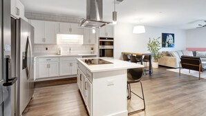 A modern kitchen with white cabinets, a stainless steel range hood, and an island with a built-in stove.