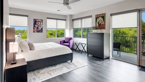 A modern bedroom with a bed, a dresser, a chair, and large windows.
