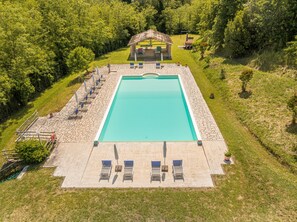 A rectangular swimming pool with a stone deck, surrounded by lounge chairs and a covered seating area.
