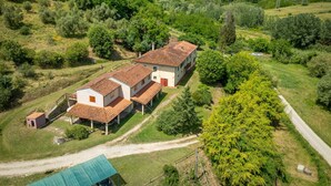 Une maison de campagne avec un toit recouvert de tuiles rouges, entourée de verdure et bordée d’un chemin de terre.