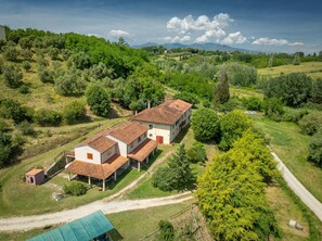 A rural house with a red-tiled roof, surrounded by greenery and a dirt path.