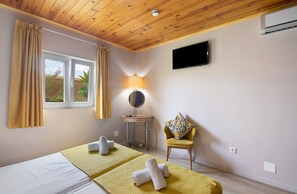 Una habitación con cama, una silla, televisor, lámpara y ventana con cortinas.