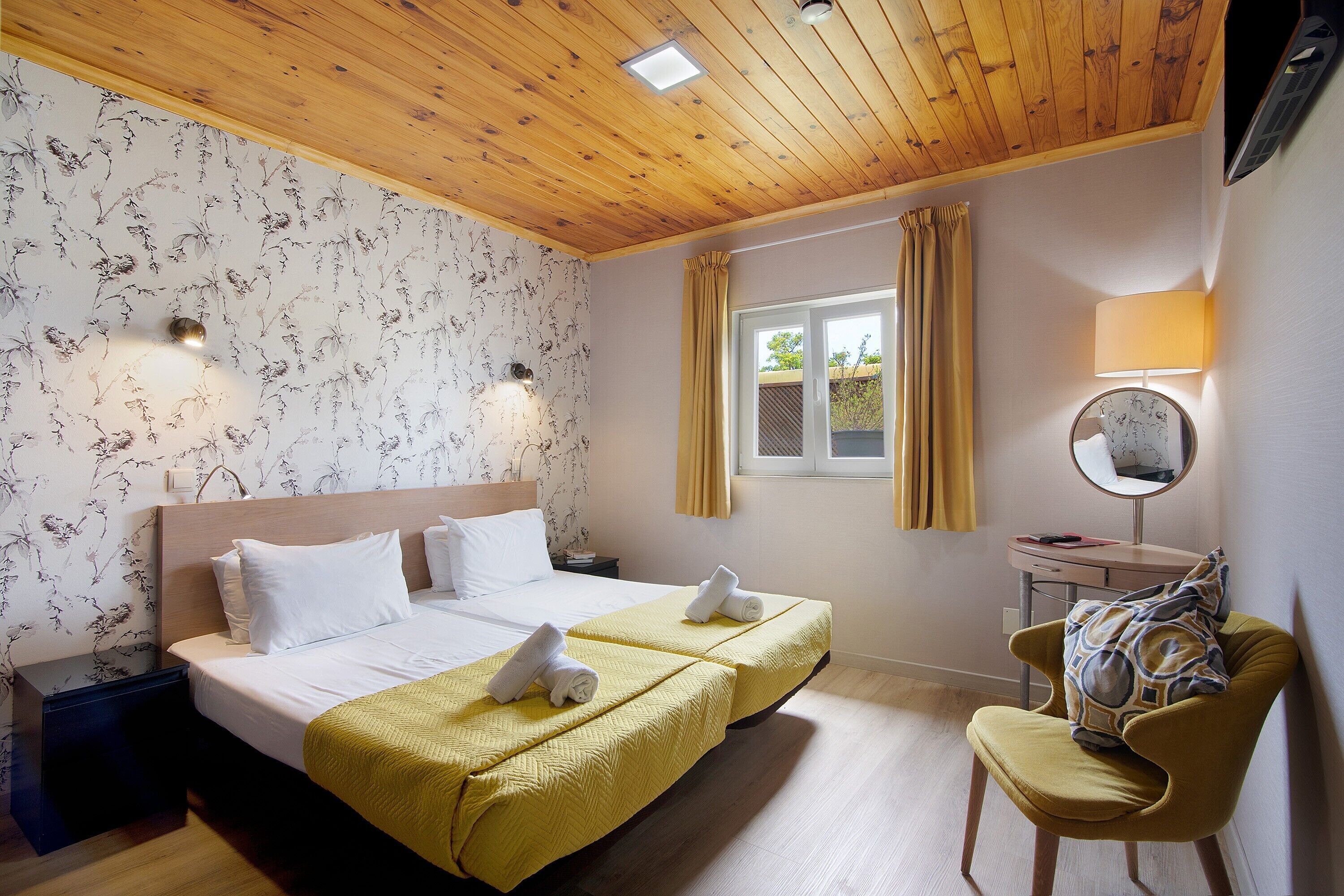 Une chambre d’hôtel avec deux lits, une chaise, un bureau, un miroir et une fenêtre avec des rideaux.