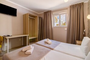 A hotel room with two beds, a desk, a TV, and a window with curtains.