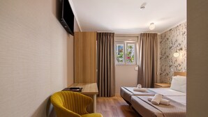 Une chambre d’hôtel équipée d’un lit, d’un bureau, d’une chaise, d’une fenêtre avec des rideaux et d’un téléviseur fixé au mur.