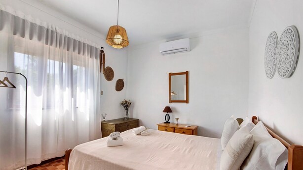 A neatly arranged bedroom with a bed, bedside table, lamp, and a hanging light fixture. - Holiday Home 'Casa Maria Beatriz' with Private Terrace, Private Garden and Wi-Fi (Vila Nova de Cacela)