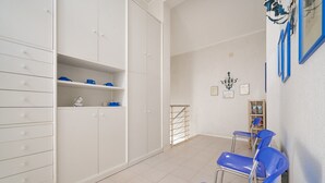A room with a white wardrobe, blue chairs, a small shelf with items, and a wall-mounted light fixture. - Holiday Home 'Villa Liberty Rosa' with Sea View, Wi-Fi and Air Conditioning (San Vincenzo)
