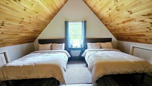Una habitación con dos camas, una ventana y techos inclinados de madera.