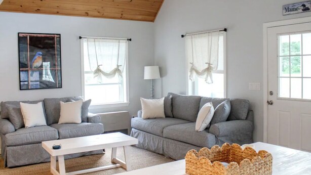 Una sala de estar acogedora con dos sofás grises, una mesa de centro blanca y un cesto decorativo.