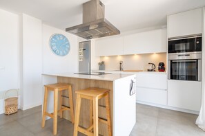 Une cuisine moderne dotée d’un îlot central, de tabourets de bar, d’une hotte en acier inoxydable, d’une horloge et d’appareils électroménagers intégrés.