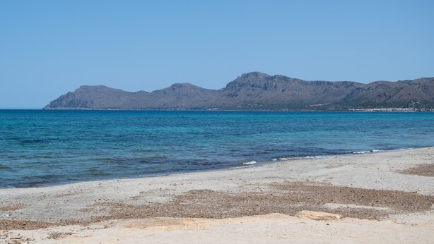 Une plage avec une eau d’un bleu limpide et une montagne en arrière-plan.