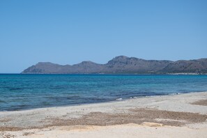 Une plage avec une eau d’un bleu limpide et une montagne en arrière-plan.