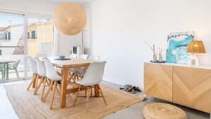 Un espace repas moderne avec une table en bois, des chaises blanches, un tapis tissé et un luminaire suspendu.