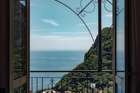 A balcony with a view of a coastal landscape, including a body of water and a hill with vegetation.