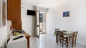 A kitchen with a stove, a microwave, and a table with chairs. There is a TV mounted on the wall and a window with curtains.