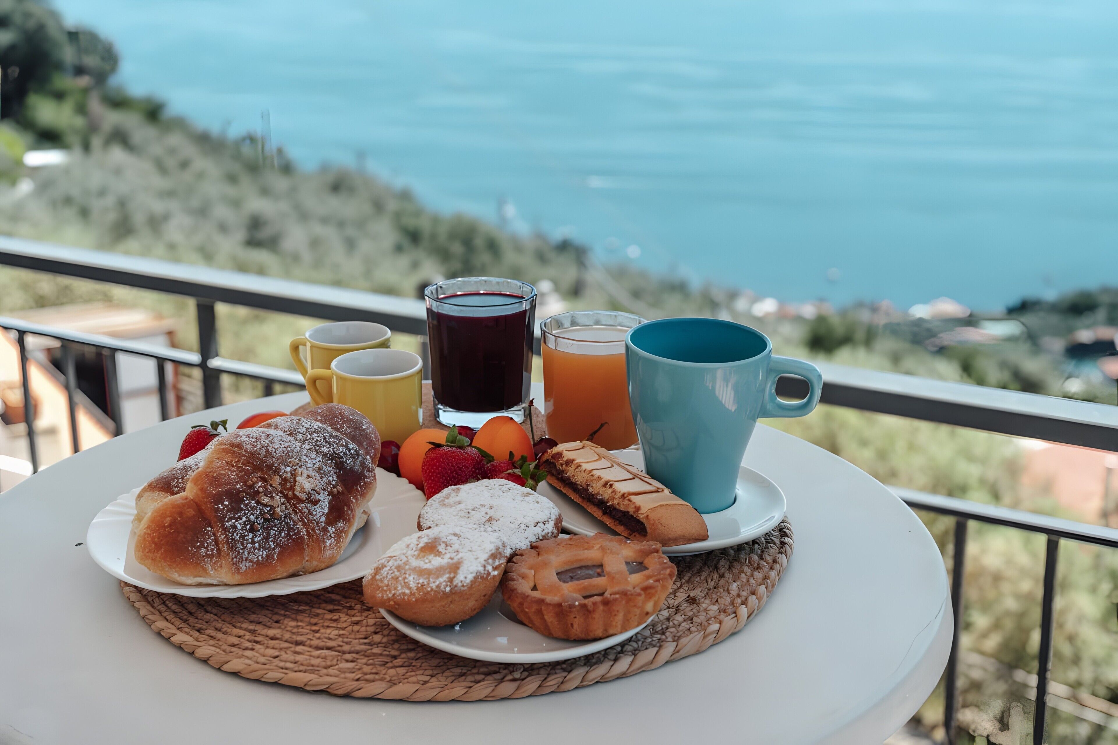 Uma mesa com itens de café da manhã, como pães, frutas e bebidas, emoldurada por uma paisagem deslumbrante.