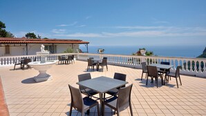 A terrace with a table and chairs, a fountain, and a view of the sea.