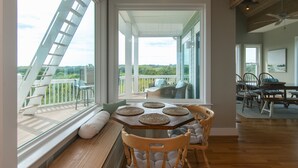 A dining area with a view of the outdoors, a wooden table with placemats, cushioned chairs, and a bench with pillows. - Tequila Sunset:Amazing Dog Friendly Home;Ocean Views/Private Dock; Minutes to Beach;Elevator/WiFi (Edisto Island)