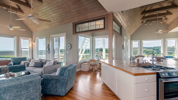 A spacious living area with a kitchen, large windows, and a balcony. - Tequila Sunset:Amazing Dog Friendly Home;Ocean Views/Private Dock; Minutes to Beach;Elevator/WiFi (Edisto Island)