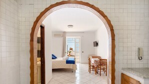 A room with a bed, a desk, and a chair, connected by an arched doorway.