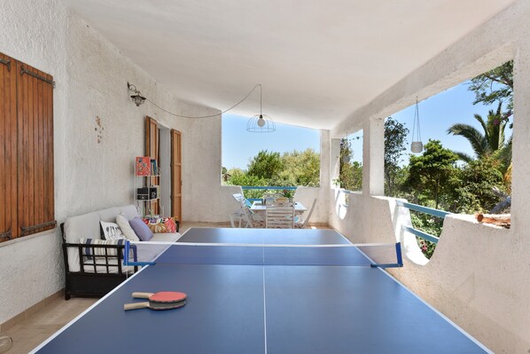 Una habitación con mesa de ping pong, sofá y vista a árboles.