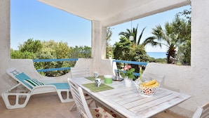 Ein Balkon mit zwei Liegestühlen, einem Tisch mit einer Bananenkiste, einer grünen Tasse und einer weißen Tasse.