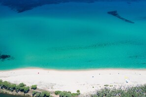 Vista aérea de una playa con agua turquesa cristalina, una orilla arenosa y vegetación escasa.