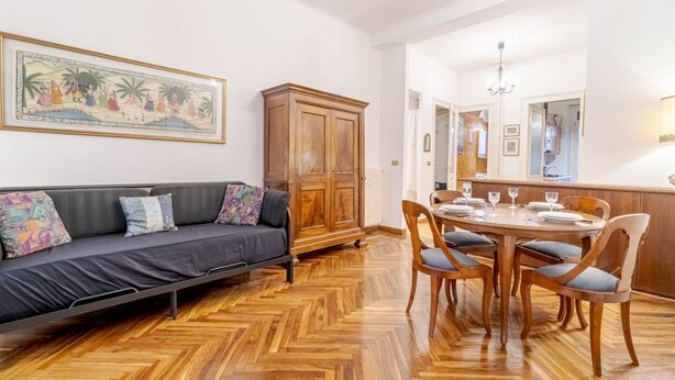 A room with a sofa, dining table, chairs, a cabinet, and a chandelier. - GuestHost - Torino Old Fashion Apartment with Balcony (Torino)