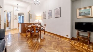 A dining area with a wooden herringbone floor, a chandelier, framed artwork, and a television on a stand. - GuestHost - Torino Old Fashion Apartment with Balcony (Torino)