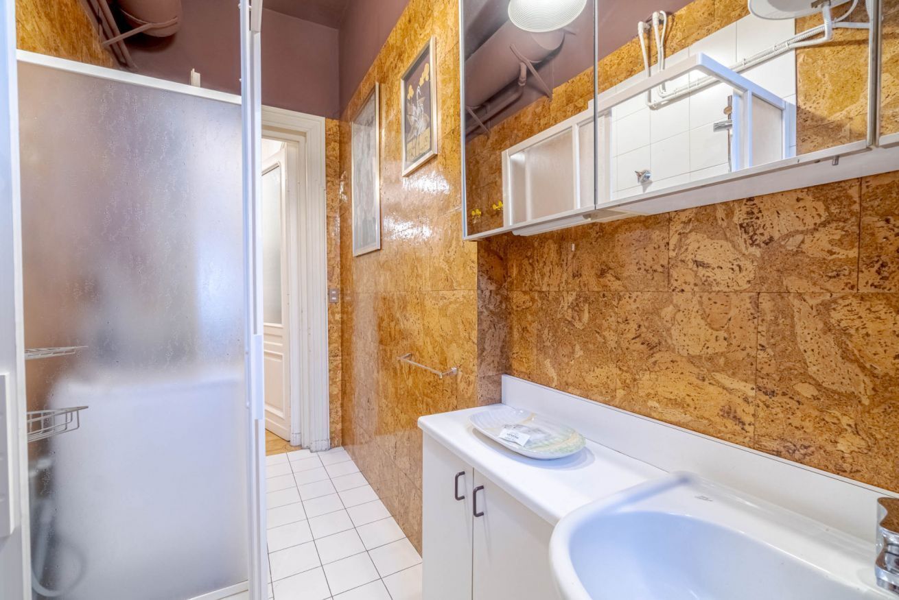 Une salle de bain avec une douche à parois de verre, un lavabo blanc, un miroir et un mur en marbre.
