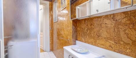Une salle de bain avec une douche à parois de verre, un lavabo blanc, un miroir et un mur en marbre.