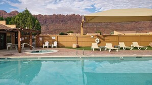A pool area with lounge chairs and a covered seating area, surrounded by a wooden fence and a mountain backdrop. - Moab Rim Village 2BR condo w/ pool & red rock view (Moab)