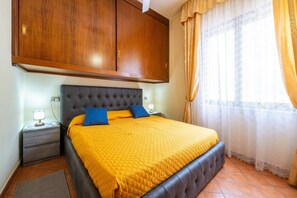 Une chambre à coucher comprenant un lit, des tables de chevet, une armoire et une fenêtre avec des rideaux.