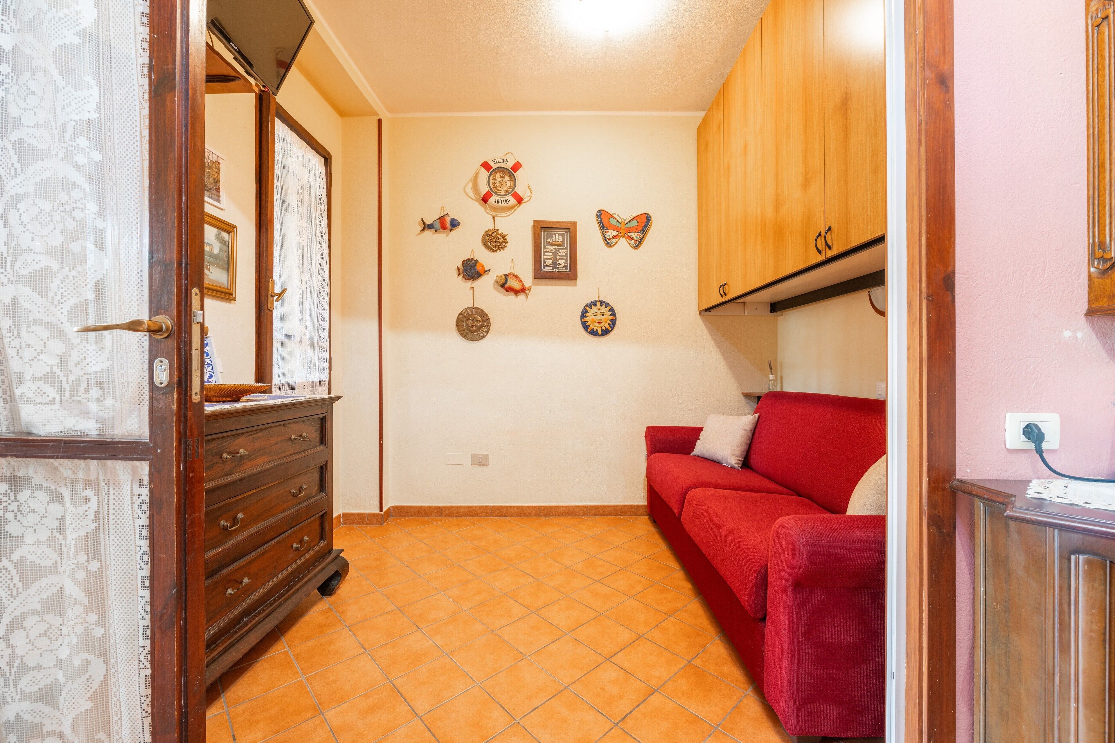 A room with a red sofa, wooden cabinets, a tiled floor, and wall decorations including fish, a butterfly, and a framed picture.