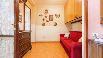 A room with a red sofa, wooden cabinets, a tiled floor, and wall decorations including fish, a butterfly, and a framed picture.