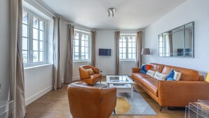 Un salon moderne avec un canapé en cuir marron, un fauteuil assorti, une table basse en verre et un grand miroir au mur.