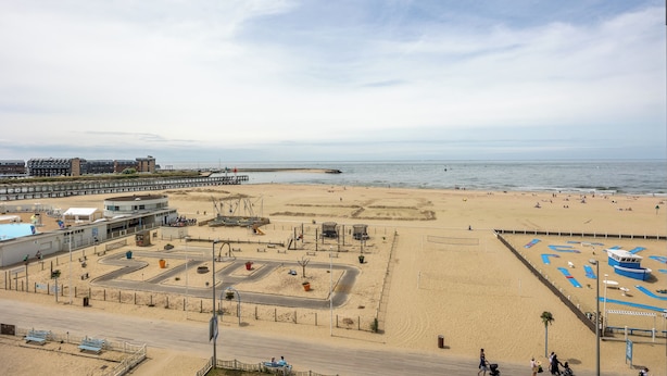 Une plage avec une promenade en bord de mer, un espace de stationnement et un poste de surveillance pour les sauveteurs.