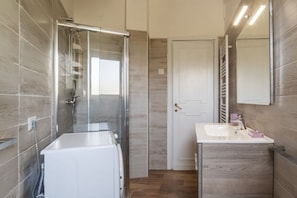 A modern bathroom with a glass shower enclosure, a white sink, and a door with a towel rack. - GuestHost - 4 Winds Holiday Rental (Roma)