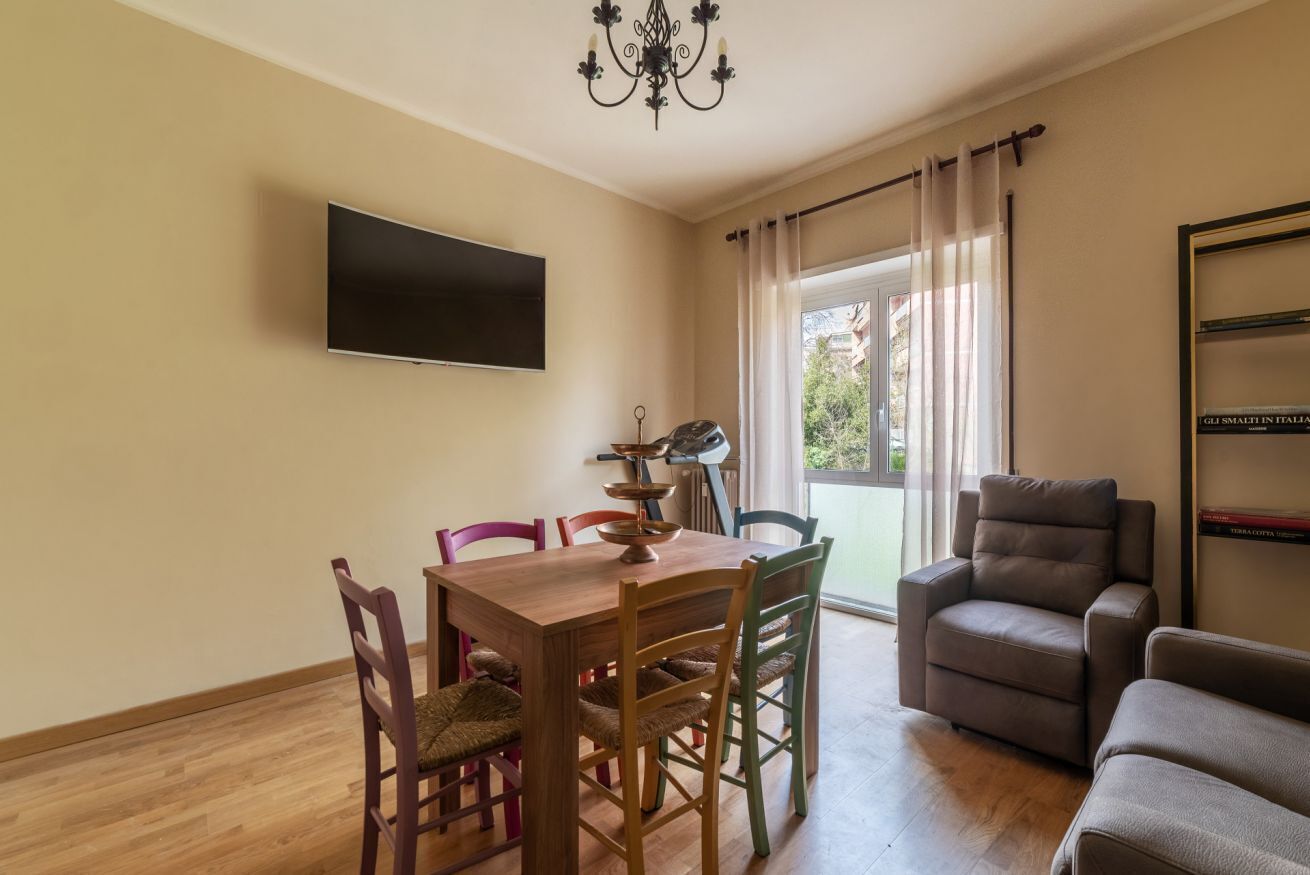 A living room with a flat-screen TV, a dining table with chairs, a sofa, and a window with curtains.