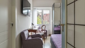 A bedroom with a bed, a desk, a chair, a TV, and a window with a view of buildings. - GuestHost - 4 Winds Holiday Rental (Roma)