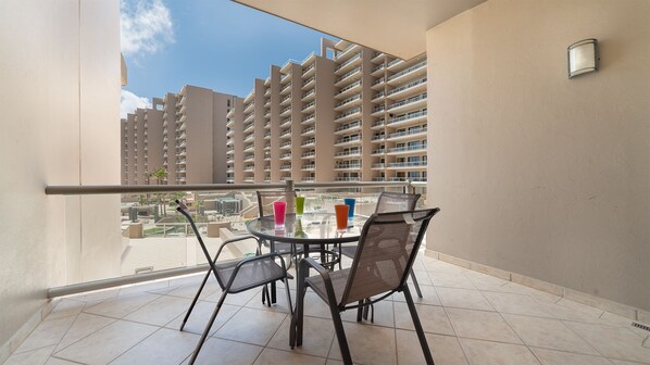 Un balcon avec une table et des chaises en verre, donnant sur un immeuble de grande hauteur.