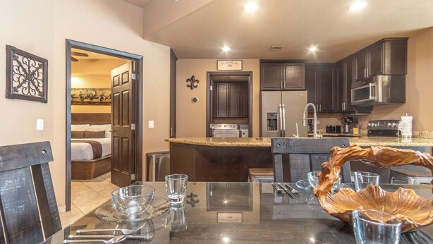 A modern kitchen with dark cabinetry, stainless steel appliances, and a glass dining table with cutlery. - Las Palomas Phase I Topaz 202 Exceptional OceanView 1BR 1BA Unit. (Puerto Peñasco)