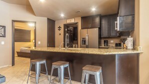 A modern kitchen with dark wood cabinets, a granite countertop, stainless steel appliances, and three bar stools. - Las Palomas Phase I Topaz 202 Exceptional OceanView 1BR 1BA Unit. (Puerto Peñasco)