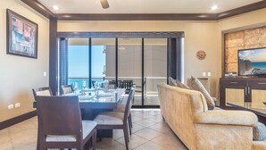 A dining area with a table set for four, a sofa, and a television on a cabinet. - Las Palomas Phase I Rubi 901 Exceptional OceanView 3BR 3BA Unit (Puerto Peñasco)