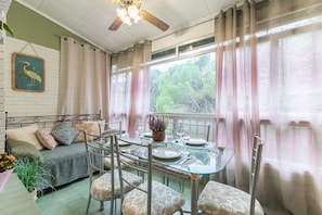 A dining area with a glass table, metal chairs, a green sofa, and a ceiling fan.